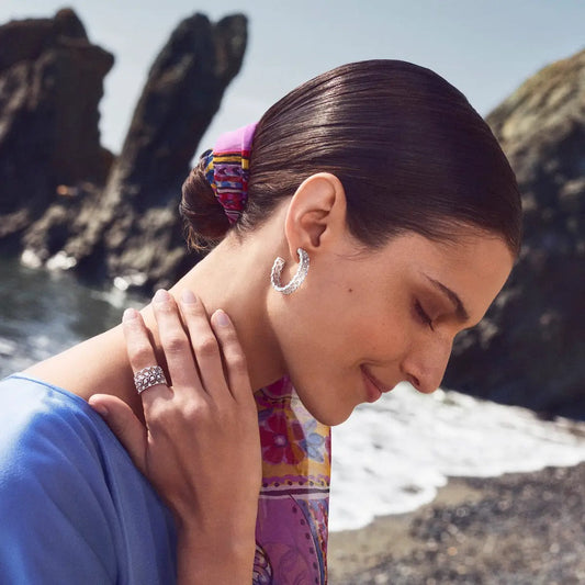 Model wearing Buccellati diamond hoop earrings and a Buccellati diamond band ring by the ocean.