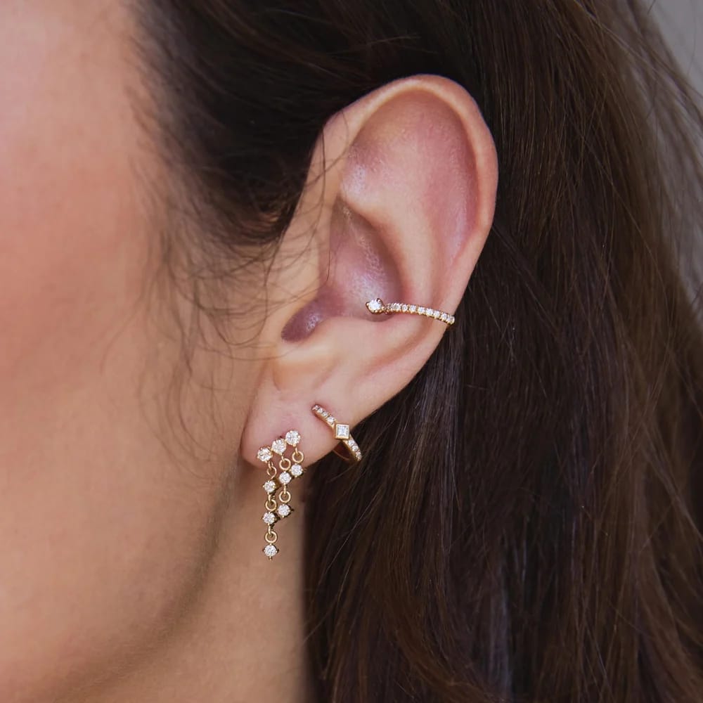 14K GOLD HUGGIE HOOP EARRINGS WITH A BEZEL SET PRINCESS DIAMOND IN THE MIDDLE AND 4 WHITE PAVE DIAMONDS ON EACH SIDE